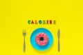 Calories and Pink donut on blue plate and knife fork on yellow background.