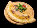 Calzone pizza on a round wooden board isolated on black background.