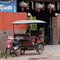 A little Asian girl sits in a moto rickshaw near a house with red lanterns