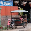 Little Asian girl sits in a moto rickshaw near a house with red lanterns