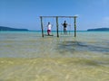 Cambodian Asian Man & Woman Standing on Swings in the Ocean