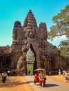 Tuk tuk drives through Angkor stone face gate Royalty Free Stock Photo