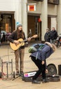 Cambridge, UK: April 2023: A busker singing and playing guitar in Cambridge and person placing money into a guitar case