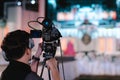 [camcorder while filming] Video camera operator working with his equipment, Cameraman recording male speaker wearing suit at media Royalty Free Stock Photo