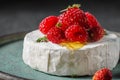 Camembert or brie cheese with wild berries, honey and thyme on dark background. French appetizer dessert
