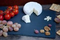 Camembert cheese on a black stone plate with tomatoes, crackers, nuts and grape Royalty Free Stock Photo