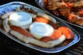 Camembert cheese, bratwurst and sausages prepared on alluminium plate for barbecue, grilled chicken breast in background