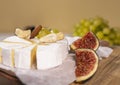 Camembert cheese on wooden board, branch of green grapes , slice of figs and nuts.