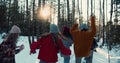 Camera follows group of excited happy friends run through snowy winter forest on sunny Christmas vacation slow motion.