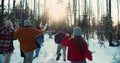Camera follows group of excited happy friends run through snowy winter forest on sunny Christmas vacation slow motion.