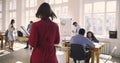 Camera follows middle aged business assistant woman in red dress entering large trendy loft office talking to colleagues