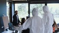 Camera follows two healthcare workers in white medical suits enter office business meeting, close it during COVID-19.