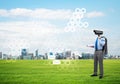 Camera headed man standing on green grass against modern cityscape