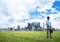 Camera headed man standing on green grass against modern cityscape