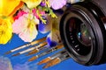 Camera lens, summer flowers and artist`s brushes. The lens is an optical device for creating an optical image. Garden summer