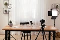 Camera and lighting equipment on tripods near table in room. Blogger workplace