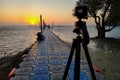 Camera mounted on a tripod shooting a coupe on the pier and sunrise under the sea. Focus on man and woman Royalty Free Stock Photo