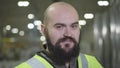 Camera moving up, portrait of bearded baldheaded Caucasian man smiling at camera. Happy worker in green vest standing at