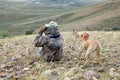 Camouflage hunter and dogs scanning arid landscape