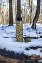 Camouflage thermos with hot tea or coffee in the forest, outdoors in the snow.