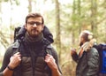 Camp, adventure, traveling and friendship concept. Man with a backpack and beard and his friend hiking in forest.