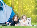 Camp in tent with children - girls sisters with little dog chihuahua sitting together near tent. Travelers sit in summer forest. Royalty Free Stock Photo