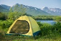 Yellow tent placed at green grass with amazing view on the river and mountains