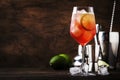 Campari tonic alcoholic cocktail with red bitter, tonic, lime and ice. Old wooden table background, bar tools, selective focus.