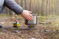 Camper is cooking dinner in a metal pan during camping. Enjoy a tasty food during hiking trips. Tourist food on a gas burner for