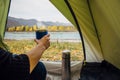 Camper holding mug with hot tea inside the green tent on the background of beautiful mountain landscape. View from inside Royalty Free Stock Photo