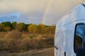 Camper van living vanlife on nature landscape with a rainbow behind it at sunset, in Portugal