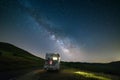 Camper van on road side in beautiful night landscape under the stars. The Milky Way galaxy arc and stars over illuminated