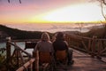 Campers Admire Sunrise at Kawah Putih, Seated on Wooden Ledge