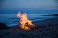 A campfire burns on a deserted sandy beach at the seashore in the evening