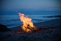 A campfire burns on a deserted sandy beach at the seashore in the evening