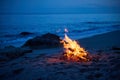 A campfire burns on a deserted sandy beach at the seashore in the evening