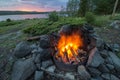 A campfire burns hot at a lakeshore campsite, as the sun sets in the mountains.