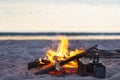 Campfire burns on the seashore next to waves during sunset