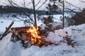 Campfire burns in the snow in the forest hill, on a background of snow covered trees and mountains campfire burning in cold winter