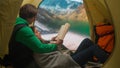 People on campsite traveling and hiking, exploring nature. Young loving couple reading a book inside the tent at lake Royalty Free Stock Photo