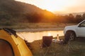 Camping at beach of mountain river. suv car. yellow tent. camp table and chairs