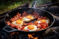 Camping breakfast with bacon and eggs in a cast iron skillet. Fried eggs with bacon in a pan in the forest Royalty Free Stock Photo