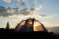 Camping at daybreak. The tent stands under blue sky with clouds in rays of morning sunlight Royalty Free Stock Photo