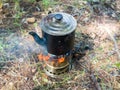 A camping kettle is heated over a fire, on a wood chip stove