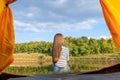 Camping on lake shore at sunset, view from inside tourist tent. Girl enjoy nature in front of tent