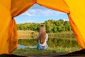 Camping on lake shore at sunset, view from inside tourist tent. Girl enjoy nature in front of tent
