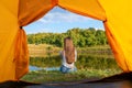 Camping on lake shore at sunset, view from inside tourist tent. Girl enjoy nature in front of tent