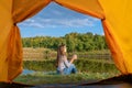 Camping on lake shore at sunset, view from inside tourist tent. Girl enjoy nature in front of tent