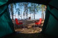 Camping in the middle of the forest, taken from inside the tent. View of the folding table and chairs with gas stove in the backgr