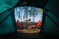 Camping in the middle of the forest, taken from inside the tent. View of the folding table and chairs with gas stove in the backgr